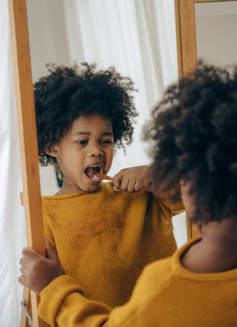 Little boy brushing his teeth in front of a mirror.