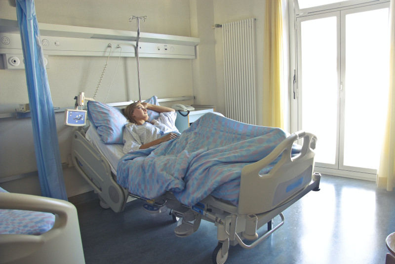 A woman lying in a hospital bed, gazing out the brightly lit window.