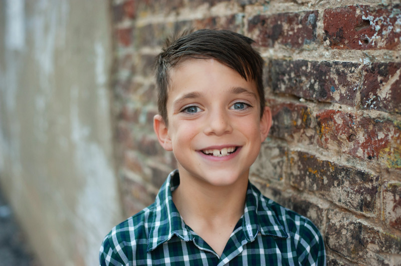 A child with prominent protruding teeth stands next to a brick wall.