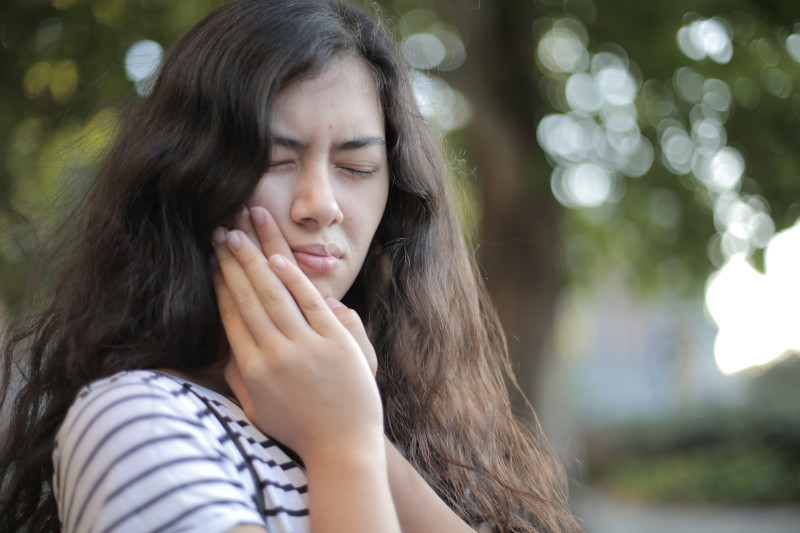 A woman placing both hands on the side of her mouth, with a look of pain on her face.